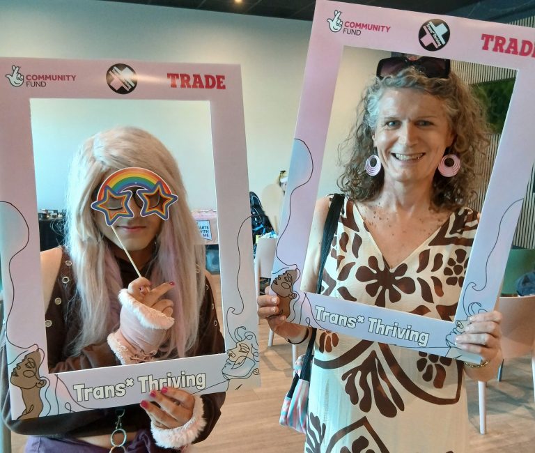 Two people pose with Trans* Thriving selfie frames.